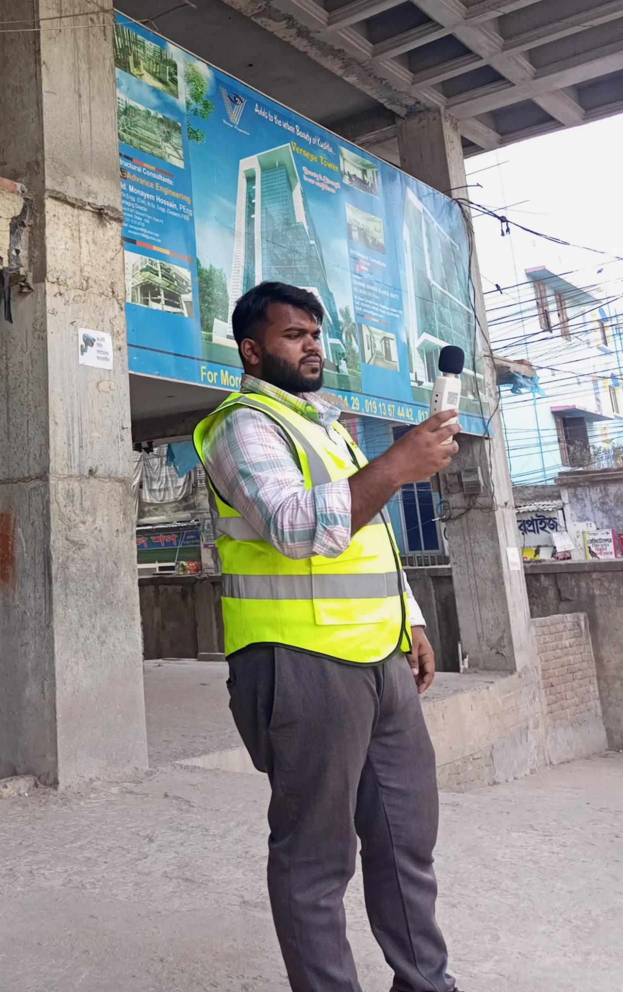 Team member wearing a high-visibility vest and holding a sound level meter at a construction site