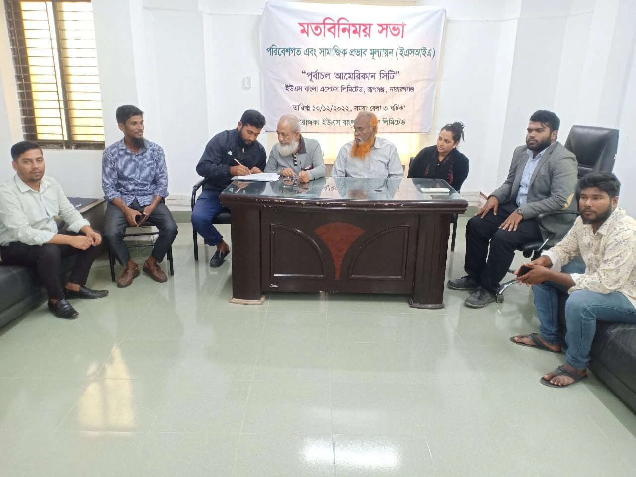 Project stakeholders seated together at a consultation meeting with an environmental and social assessment banner